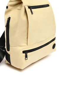 Zaino beige con esterno morbido e testurizzato, cerniere nere e una tracolla a contrasto. Include due tasche con zip per riporre gli oggetti.