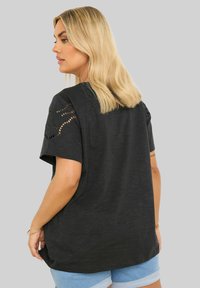 Mustapaita lyhyillä hihoilla, joissa on pitsiyksityiskohtia, rento istuvuus, pehmeä rakenne ja hieman kaareva helma, yhdistettynä vaaleansinsisiin farkkushortseihin.