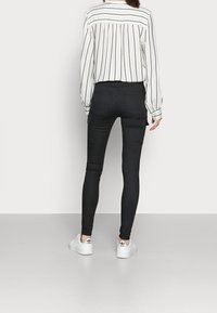 Černé slim-fit cargo kalhoty s bočními kapsami, stylizované s bílou pruhovanou blůzou a bílými teniskami. Hladká textura a přiléhavý design.