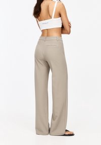 Pantalons beige à jambes larges en tissu lisse, avec une taille mi-haute et deux poches arrière. Portés avec un top court blanc.