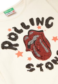 Felpa color crema con il testo in paillettes nere e rosse "ROLLING STONES" e un design di linguetta in paillettes rosse con stelle arancioni.