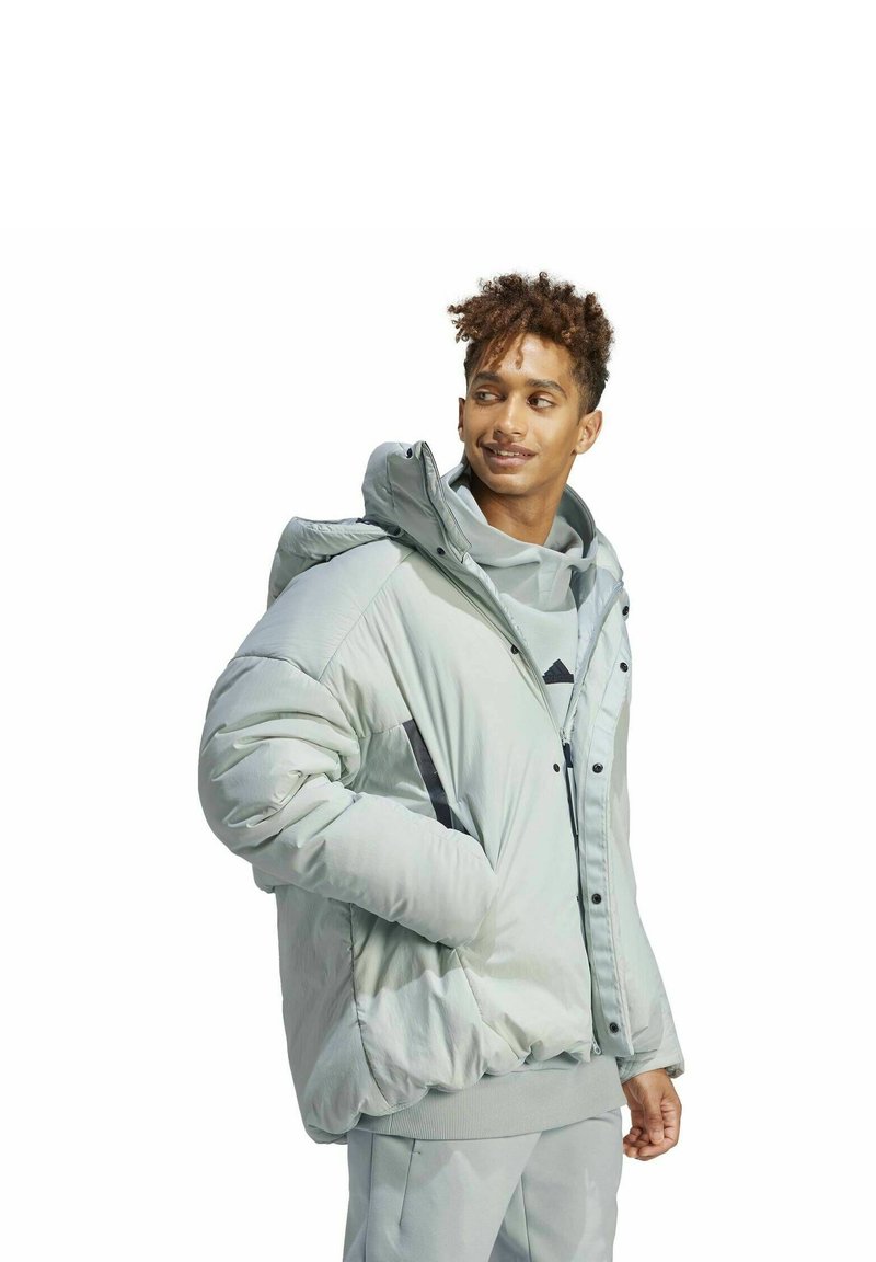 Jasnoszara kurtka puchowa z wysokim kołnierzem, zapinana na zamek, z kapturem. Posiada czarne akcenty oraz gładką, błyszczącą fakturę.