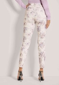 Wit met lichtpaarse en blauwe bloemen, spijkerbroeken met bloemenprint. Slank model met een hoge taille en achterzakken. Gemaakt in combinatie met zwarte hakken.
