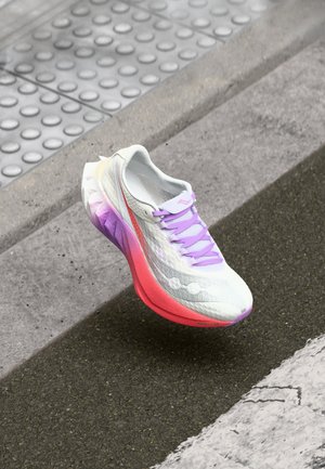 Witte hardloopschoen met een gestructureerde bovenkant, paarse veters en een verloopzool die overgaat van roze naar paars. Opvallende merkaccenten zichtbaar.