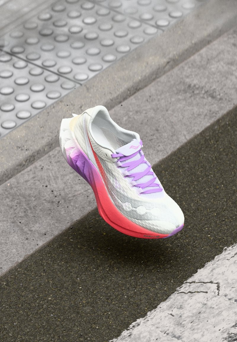 Scarpa da corsa bianca con tomaia testurizzata, lacci viola e suola a gradiente che passa dal rosa al viola. Accenti di branding ben visibili.
