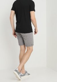 Harmaat puuvillahousut, joissa on käännetyt lahkeet, yhdistettynä harmaisiin ja valkoisiin lenkkikenkiin. Mallilla on päällään tiukka musta t-paita, joka näkyy takaa.