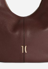 Borsa in pelle marrone dalla texture strutturata con una forma curva, chiusura con zip e dettagli in oro con un design numerico e astratto.