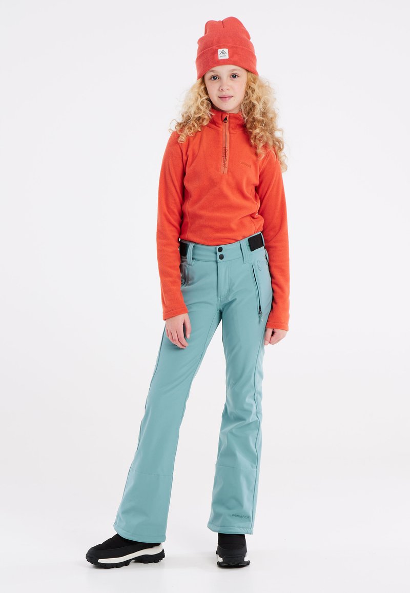 Fleece pullover in feloranje, half-zip stijl; gecombineerd met lichtblauwe skibroek met ritszakken en een aangesloten tailleband; zwarte laarzen.