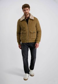 Katoenen jasje in camel kleur met een beige schapenwollen kraag, ritssluiting, twee voorzakken en geribde manchetten, gedragen met donkere jeans en sneakers.