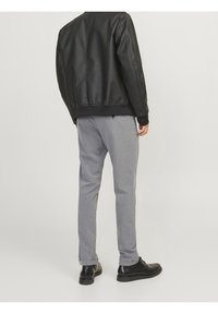 Veste en cuir synthétique noir, pantalon gris ajusté et chaussures noires. La veste présente des bords côtelés et des poignets, tandis que le pantalon a une texture subtile.