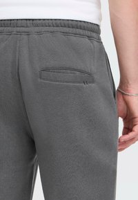 Grå joggebukser med en myk tekstur, elastisk midje og en liten lomme bak, med synlige sømdetaljer.