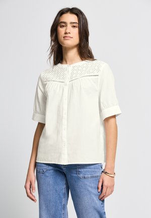 Blouse blanche à manches courtes avec fermeture à boutons et accents brodés sur le yoke. Fabriquée en tissu léger avec une coupe fluide.
