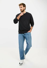 Zwarte sweatshirt met geribbelde mouwen en halslijn, gecombineerd met lichtblauwe recht-zittende jeans en witte sneakers met zwarte accenten.