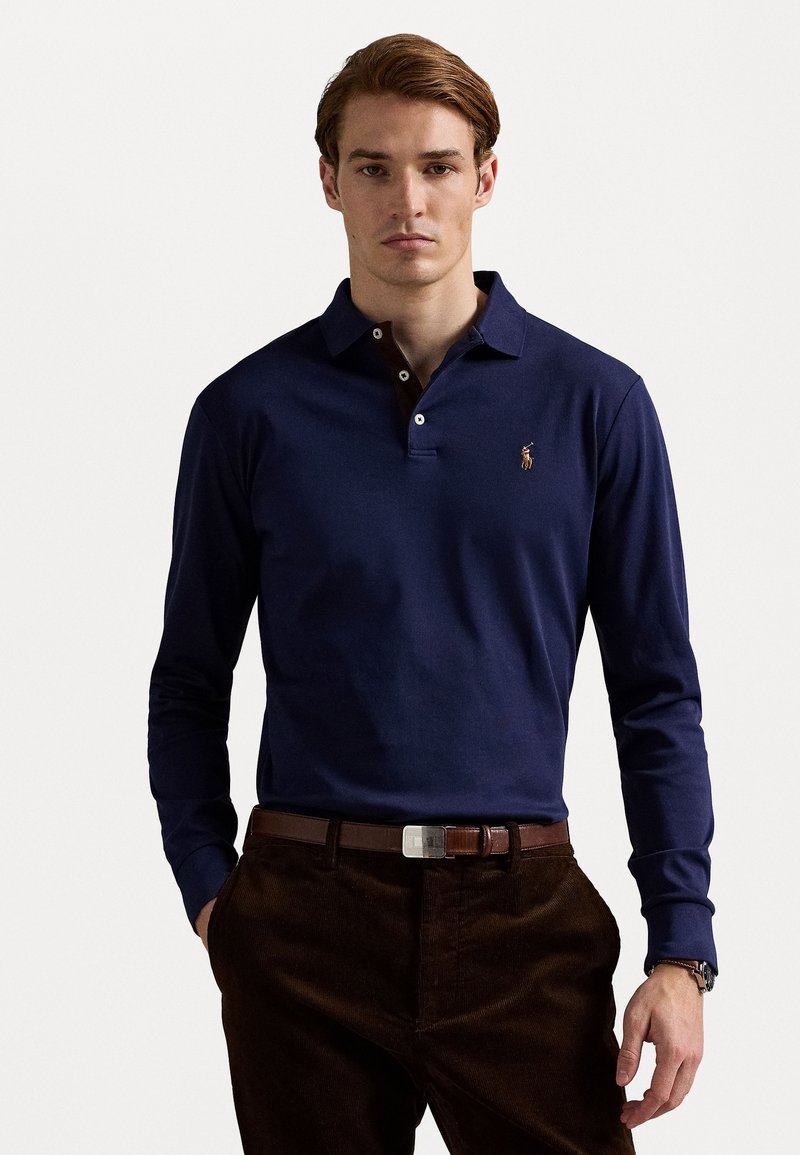 Dark navy long-sleeve polo shirt with two-button collar and embroidered logo on left chest, paired with brown corduroy pants and a belt.