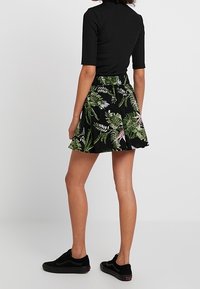 Jupe noire à imprimé floral vert et violet, coupe évasée, avec une ceinture élastique. Associée à un haut noir ajusté et des baskets noires.