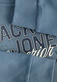 Mėlynas džemperis su įrengtomis rankovėmis ir dideliu grafiniu spausdinimu su „Jack & Jones“ baltu ir tamsiai mėlynu tekstu. Minkšta medžiagos tekstūra.