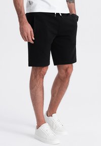 Shorts neri in cotone con vita regolabile, dotati di tasche laterali e design aderente. Abbinati a sneakers bianche in pelle.