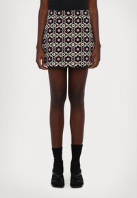 Minirock mit Blumenmuster in Pink-, Schwarz- und Cremefarben. Verfügt über einen elastischen Bund und ein enges Design. Kombiniert mit schwarzen Kniestrümpfen und Schuhen.