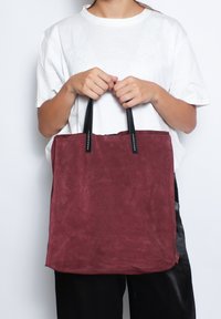 Borsa tote in suede bordeaux con manici in pelle nera, forma rettangolare, design minimale e cuciture a vista.