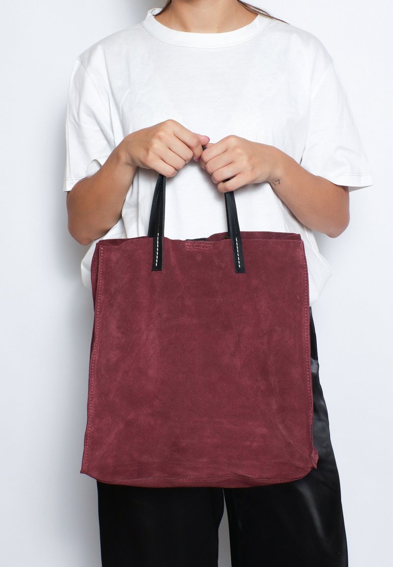 Borsa tote in suede bordeaux con manici in pelle nera, forma rettangolare, design minimale e cuciture a vista.