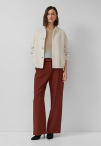 Beige fuzzy jas met gouden knopen, licht gebreid topje en brede rode broeken. Bevat een effen kleur en een gestroomlijnde silhouet. Zwarte hoge hakken.