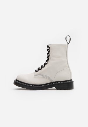 Bottine blanche en cuir à lacets, semelle noire, œillets noirs et languette au talon sur fond blanc uni.