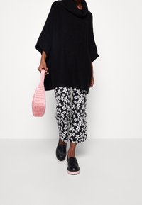 Czarny sweter w kapturze, spodnie w czarno-białe kwiaty z krótkimi nogawkami, czarne mokasyny z różowymi podeszwami oraz różowa pleciona torebka.