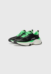 Zwarte sport sneakers met groene accenten, gemaakt van mesh en synthetische materialen, met een chunky witte zool en een zwarte rubberen outsole.