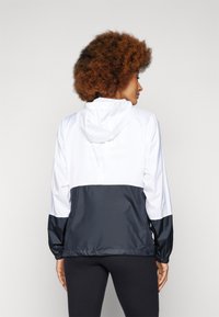 Kapuzensportjacke mit oberer Sektion in Weiß und unterer Sektion in Dunkelblau. Elastische Bündchen und Saum, aus leichtem Stoff gefertigt.