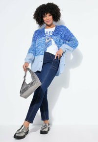 Pletený svetr s knoflíky v přechodu modré, doplněný světle modrými akcenty, v kombinaci s bílým tričkem s grafikou, tmavě modrými džínami a stříbrnými metalickými botami.