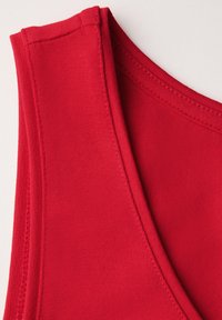 Top sportivo in tessuto rosso con scollatura arrotondata, spalline sottili e cuciture piatte. Texture liscia con colore uniforme in tutto il capo.