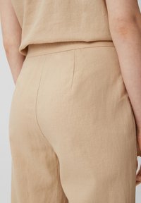 Beige Leinenhose mit entspannter Passform. Verfügt über eine glatte Textur, eine senkrechte Naht und einen elastischen Bund, der mit "CASUAL IDENTITIES" geprägt ist.