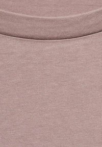 Tissu tricoté rose pâle avec une surface lisse et texturée et un col à côtes. Le matériau semble doux et extensible.