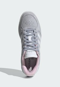 Sivá semišová teniska s bielymi tromi pásikmi, ružovými akcentmi na golieri a textúrovanou gumovou podrážkou. Zapínanie na šnúrky a logo na jazyku.