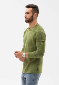 Groene blouse met lange mouwen, gemaakt van zacht materiaal, met een ronde hals en een klein merklabel aan de onderzijde, gecombineerd met lichte denim jeans.