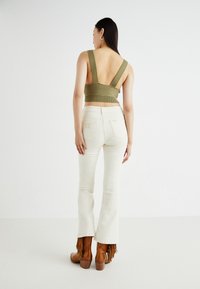 Olive green ribbed crop top with wide straps, paired with white flared jeans. Brown fringe-embellished ankle boots complete the look.