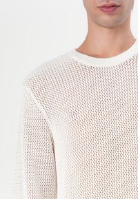 Biały sweter dziewiarski z otwartym wzorem siateczkowymi, okrągłym dekoltem i prążkowanymi mankietami. Lekki materiał zapewnia wentylację.