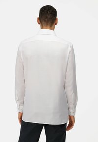 Witte lange mouwen shirt met een klassieke kraag, gladde textuur en knoopmanchetten. De achterzijde benadrukt de getailleerde pasvorm en gebogen zoom.