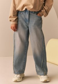 Jasnoniebieskie dżinsy typu wide-leg z postrzępionym szwem bocznym, połączone z beżowym swetrem i białymi sneakersami.