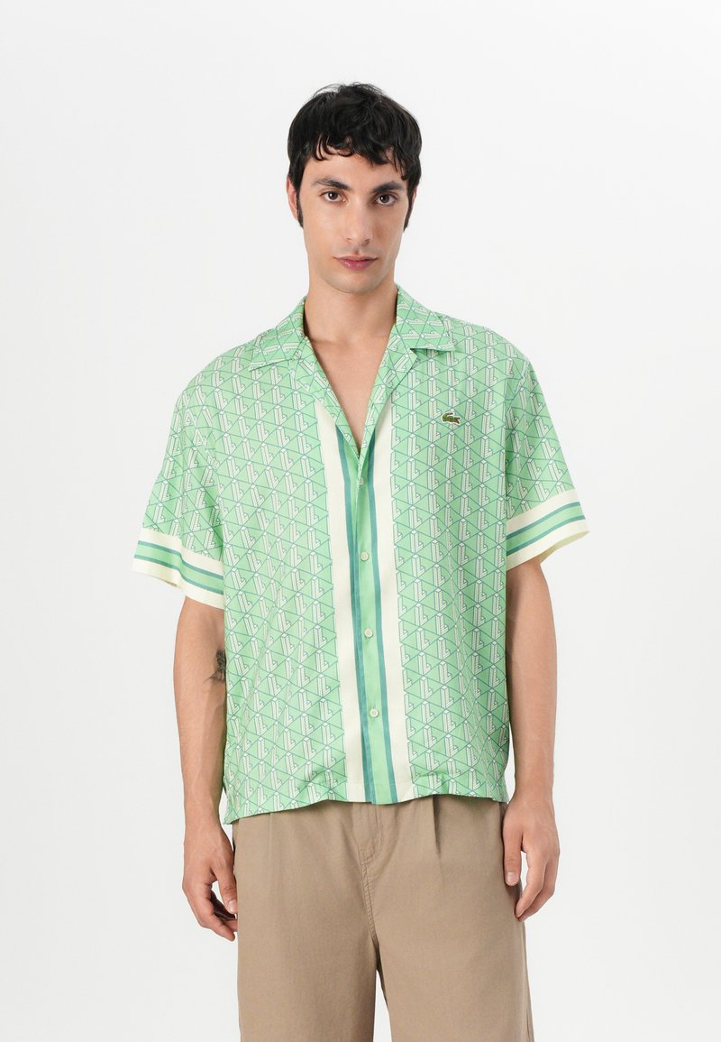 Short-sleeve green shirt featuring a geometric pattern with light green and white stripes, made of a smooth, lightweight fabric. Buttons at front.
