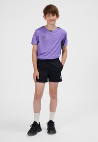 Maglietta sportiva viola a maniche corte con accenti neri, abbinata a pantaloncini neri. Scarpe nere e calzini bianchi visibili. Logo su maglietta e pantaloncini.