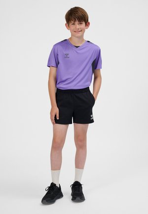 Lila Sportshirt mit kurzen Ärmeln und schwarzen Akzenten, kombiniert mit schwarzen Shorts. Schuhe sind schwarz, weiße Socken sind sichtbar. Logo auf dem Shirt und den Shorts.