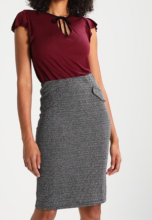 Femme portant une jupe crayon gris à chevrons ajustée avec une petite poche latérale et un haut bordeaux à manches courtes avec un décolleté en forme de goutte.