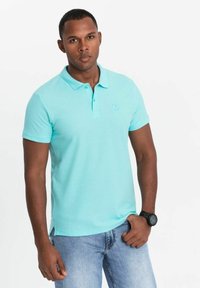 Polo bleu clair avec un col standard, des manches courtes et un petit logo brodé sur la poitrine, associé à un jean bleu.