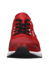 Chaussure de sport rouge avec une tige en tissu, des lacets noirs, des clous argentés sur les côtés, et une semelle en caoutchouc noire et blanche.