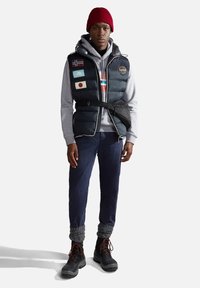 Gilet imbottito con toppe. Blu navy, con una felpa grigia sotto. Pantaloni scuri, scaldamuscoli in maglia grigia e stivali neri con lacci arancioni.