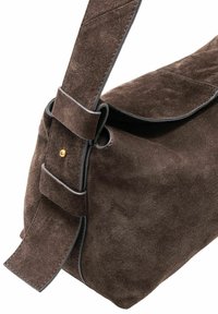 Brązowa skórzana torebka na ramię z szerokim paskiem, zdobiona złotymi ćwiekami, z czarnymi krawędziami na białym tle.