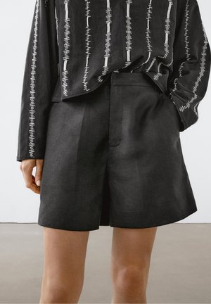 Short noir taille haute ajusté porté avec un haut noir à manches longues présentant des motifs de couture blanche verticale.