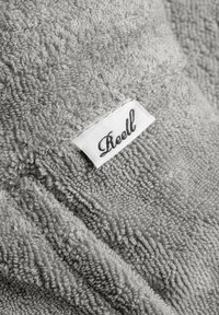 Gray towel made of soft, textured fabric, featuring a prominent stitched label with the brand name in cursive.