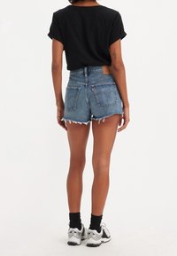 Black short-sleeve shirt paired with high-waisted denim shorts. Shorts are light blue, frayed at hem, with two back pockets and a leather tag.